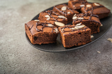 Homemade brownies with almond petals on a dark plate on a wooden background. Close up. Selective focus. Horizontal view