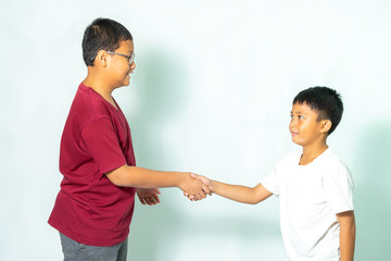 Portrait photo of two Asian boy, age 8-12, hand shake and smilling each other on white background.