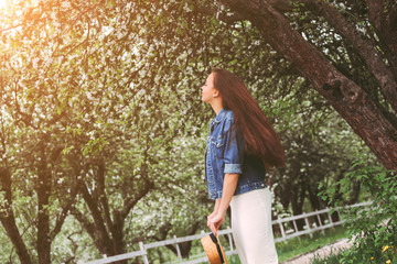 Portrait carefree young brunette girl hipster in stylish dress and denim jacket relax, walk on green countryside garden. Happy hippie woman with long hair have fun in blossom park. Enjoy spring nature