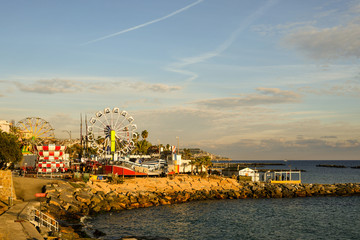 Scenic view of the amusement park on the sea shore of the coastal city with a panoramic wheel and scary carousels at sunset, Sanremo, Imperia, Liguria, Italy