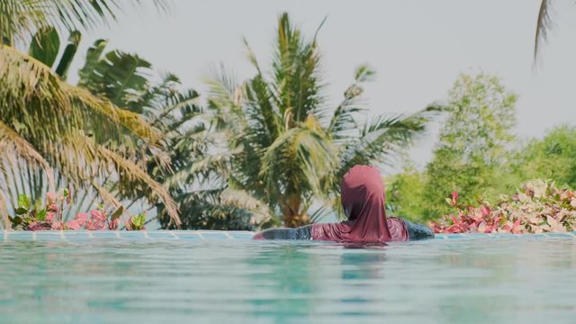 Muslim woman relaxing in swimming pool enjoying tropical nature.