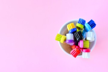 Colorful new plastic toothbrushes in white mug on pink neutral background, top view,  selective focus, copy space. Trendy health care concept 