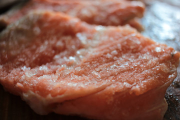 Raw salmon slices melting on a wooden cutting board. Top view of frozen pieces of red fish.
