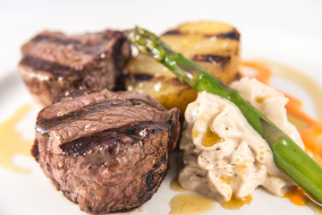 Dish of grilled beef tenderloin medallions with baked potato and asparagus