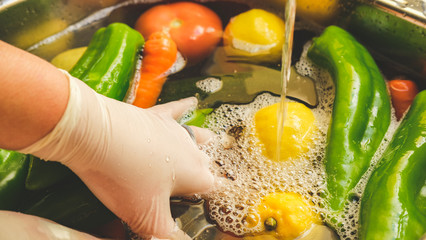A person cleaning vegetables with gloves in the sink from Virus Covid 19.