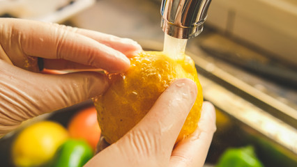 A person cleaning a lemon with gloves in the sink from Virus Covid 19.