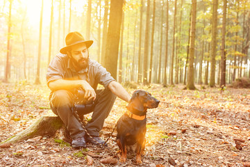 Förster mit Hund im Wald sitzt auf Baumstumpf - obrazy, fototapety, plakaty