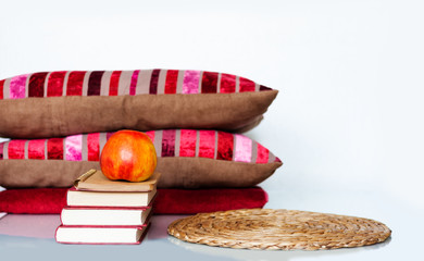 Cozy home interior decor: apple, stack of books, pillows and plaid on a white table. Distance home education. Quarantine concept of stay home.
