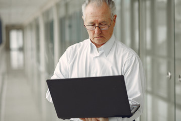 Fototapeta premium Man in the office. Old man use the laptop. Senior in a white shirt.