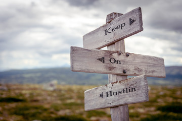 keep on hustlin text engraved on wooden signpost outdoors in nature.
