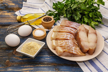 Raw fillet of saithe and frying ingredients. Fresh slices on a plate, spices, eggs, oil, breadcrumbs, parsley