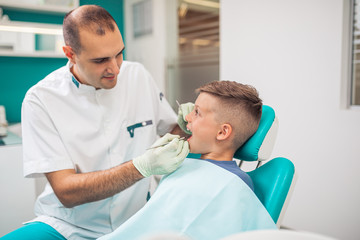 Cute little boy sitting on dental chair and having dental treatment.