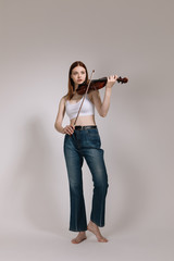 The girl in jeans and barefoot plays the violin on a white background