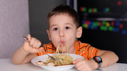 funny Little boy eat pasta in the kitchen table.