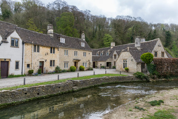 Fototapeta na wymiar English village street near the river, typical houses with stone facades and dark roofs, Castle Combe, England