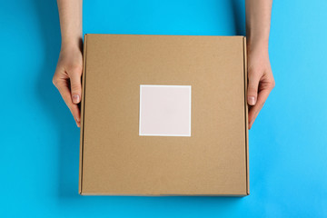 Woman holding cardboard box on light blue background, top view