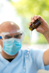 Doctor wearing a surgical mask and medical safety goggles emptying a bottle of expired liquid antibiotics. Selective focus on foreground