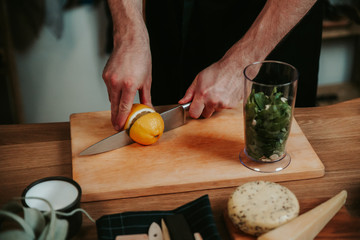 Man hands cutting lemon fruit in halve with big silver knife. 