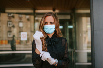 A beautiful attractive caucasian businesswoman with a mask and gloves stands in front of the company. COVID - 19 virus protection
