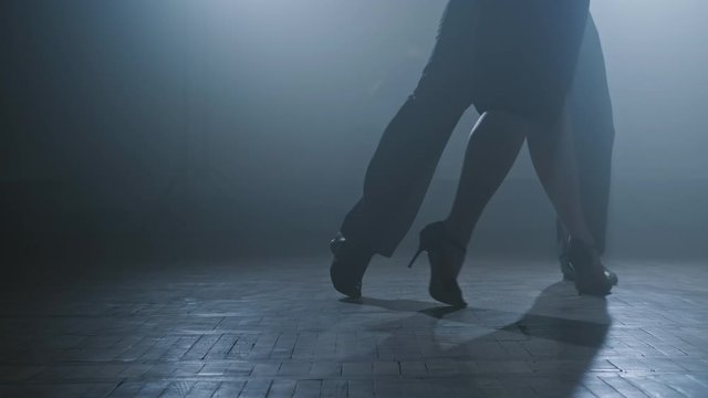 Legs of couple dancing tango in dark smoky studio in slow motion. Beautiful man and woman dancing latin dance. Close-up shot in 4K, UHD