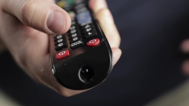 remote control close-up front view. man holding an electronic device and pressing buttons and switching channels of tv