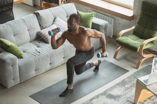 Young african-american man training at home during quarantine of coronavirus outbreak, doinc exercises of fitness, aerobic. Staying sportive during insulation. Wellness, movement concept. Sit ups.