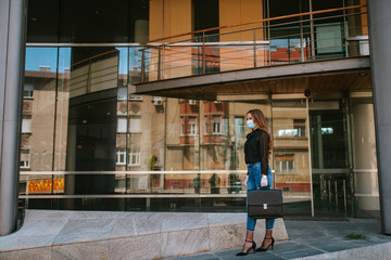 A beautiful attractive caucasian businesswoman with a mask and gloves stands in front of the company. COVID - 19 virus protection