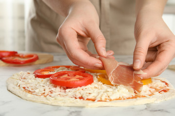 Obraz na płótnie Canvas Woman adding prosciutto to pizza white marble table, closeup