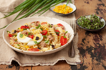Pasta salad with vegetables, egg and tuna on wooden table