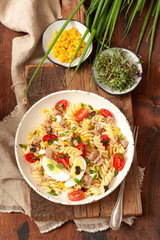 Pasta salad with vegetables, egg and tuna on wooden table
