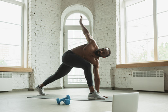 Young african-american man training at home during quarantine of coronavirus outbreak, doinc exercises of fitness, aerobic. Staying sportive during insulation. Wellness, movement concept. Stretching.