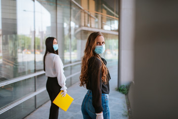 Two beautiful attractive caucasian  business women with a mask and gloves stand in front of the company. COVID - 19 virus protection