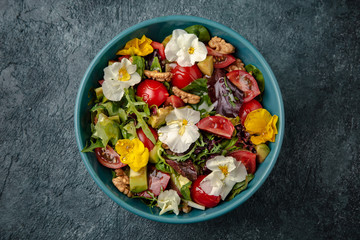 Diet vegetarian salad of cherry tomatoes, avocado, mix of greens with flowers.