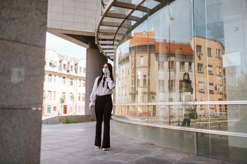 A beautiful attractive caucasian businesswoman with a mask is standing in front of the company. COVID - 19 virus protection