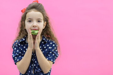 Small girl with curly hair posing for a photo holding green macaroon.