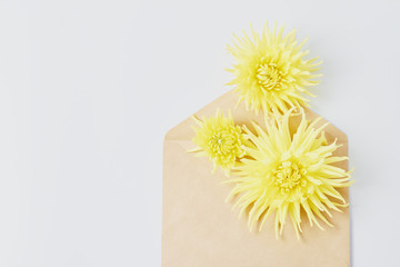 wedding concept. yellow dahlia flowers on a white desk. invitation in an envelope. flat layout, space for a text