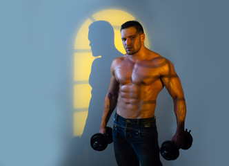 Powerful bodybuilder doing the exercises with dumbbells. Strong male with naked torso on night...