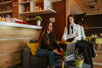 Two beautiful  caucasian business women are sitting in a cafe and working on a laptop. Work in a cafe