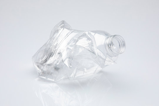 pellucid plastic bottle without cap crushed on itself, isolated in front on white background
