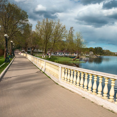 stone path with concrete railing along the lake in a country park against a beautiful cloudy sky