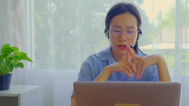 An Asian woman is teaching online via a laptop via webcam.