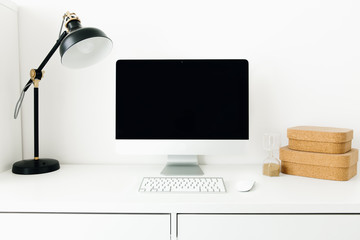 White desktop with black monitor and desk lamp. Workplace concept. Mock up blank computer screen with keyboard. Minimalism in the interior. Work at home.