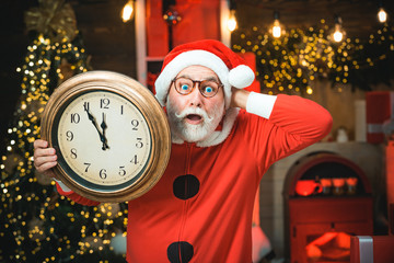 Santa Claus holding clock with countdown to Christmas or New Year Santa Claus in wooden home...