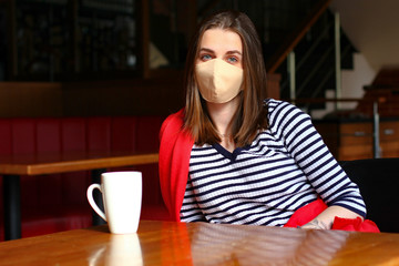 The girl in the protective medical mask is sitting in the restaurant with cup of coffee