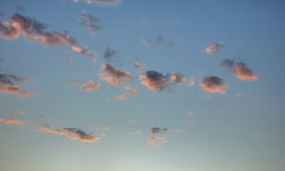 small fluffy clouds are illuminated by bright pink light by the sun's rays during sunset against a blue sky