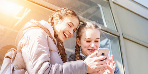 girlfriends walking together and using smartphone on street