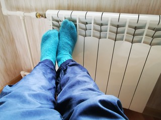 Legs in green woolen socks on a cold warm battery. The house is without heating.