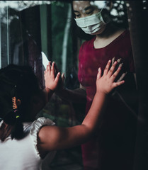 Mother wear face mask meeting daughter and touching hand through the window because of the...