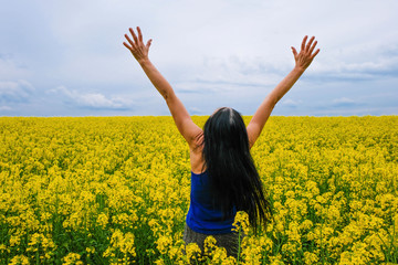Naklejka na ściany i meble 60-year-old woman in a rapeseed field. Gesture to protect the sky over Ukraine.