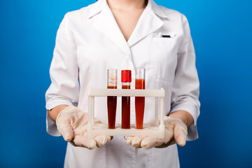 Doctor in a white medical coat standing on a blue background, holding a flask with blood in front...